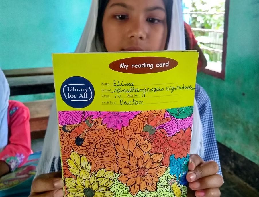 A girl holds up her Library for All reading card